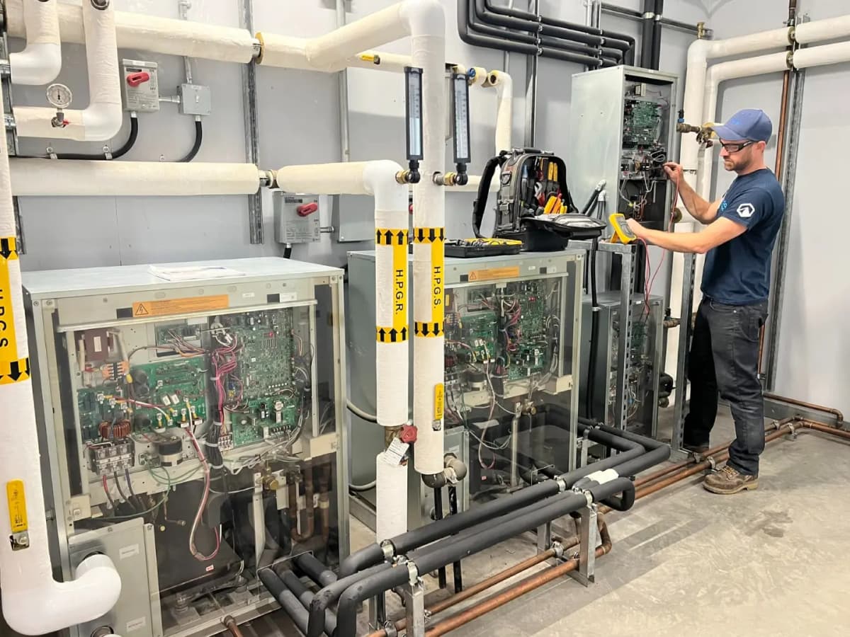 Technician servicing commercial heat pump units in a mechanical room