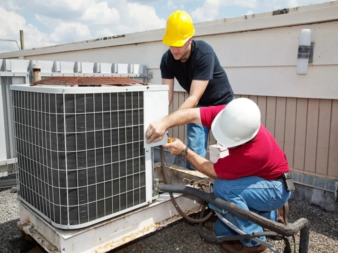 Two HVAC technicians servicing a rooftop air conditioning condenser