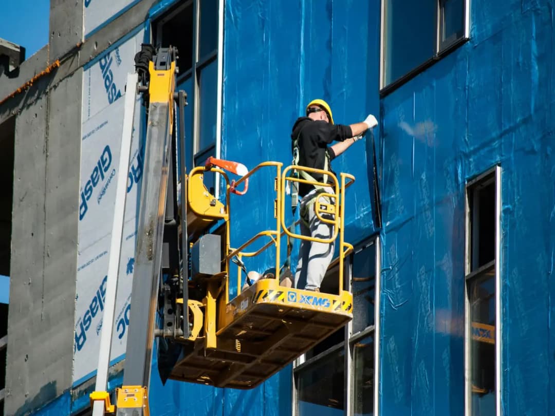 Installer on a lift fastening exterior insulation board to a building wall