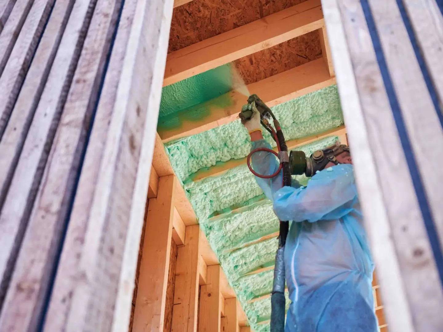 Installer spraying foam insulation between roof rafters