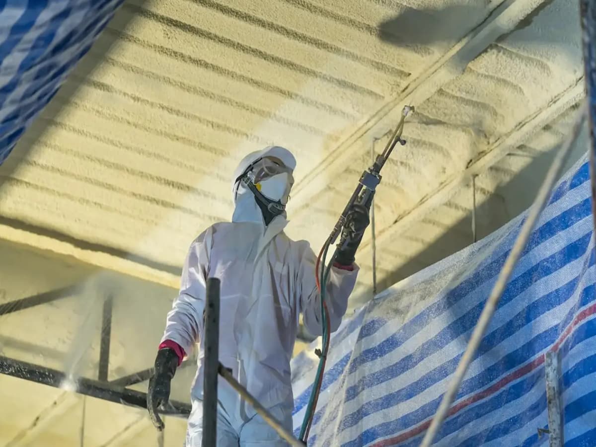 Installer in protective gear applying spray foam insulation to a ceiling